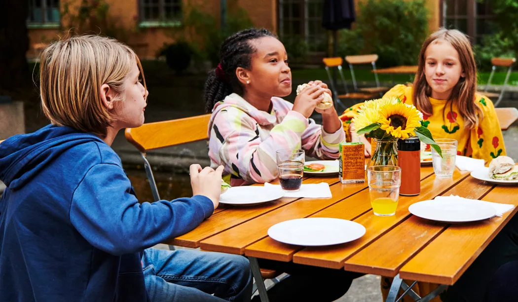 Barn som sitter vid ett bord och fikar ute på Rosengården