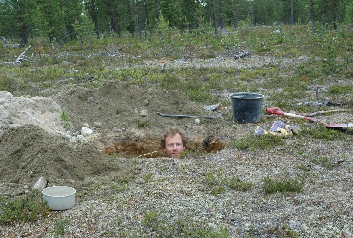 En man som grävt en grop i en skog och ställt sig i gropen.