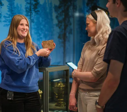 Museum educator showing an object to visitorssökare