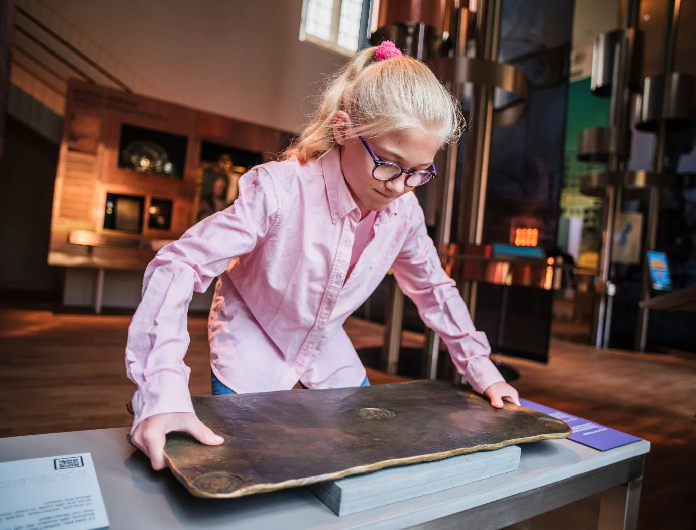 A girl tries to lift the heavy replica of a copper coin in the MONEY! exhibition