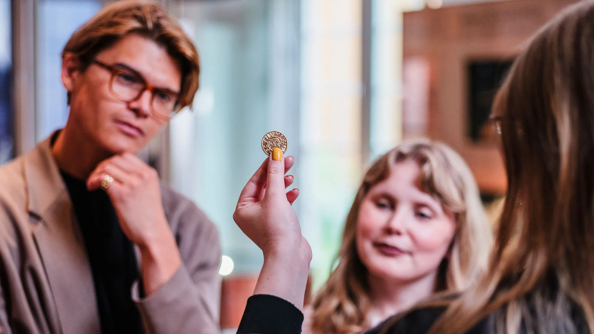 En museipedagog visar upp ett mynt för två besökare