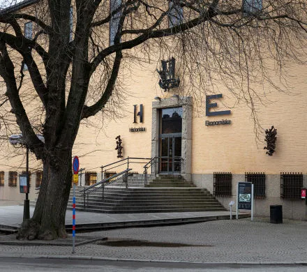 Ingången till Ekonomiska museet. Byggnadens fasad och ett träd utan löv i förgrunden.