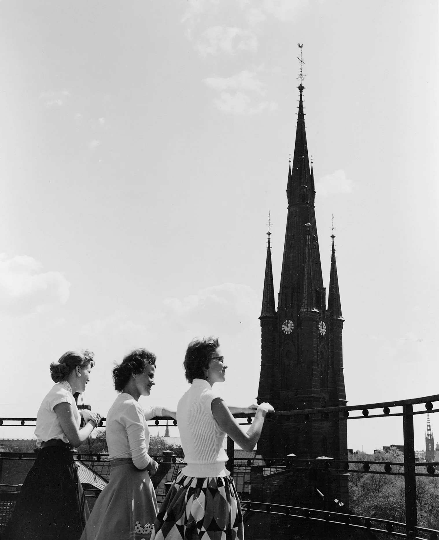 Tre kvinnor står i solen på Postgirots takterass. I bakgrunden syns Klara  kyrka.