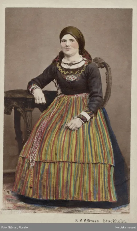 Ett färglagt fotografi på en kvinna i randig kjol och huvudduk. 