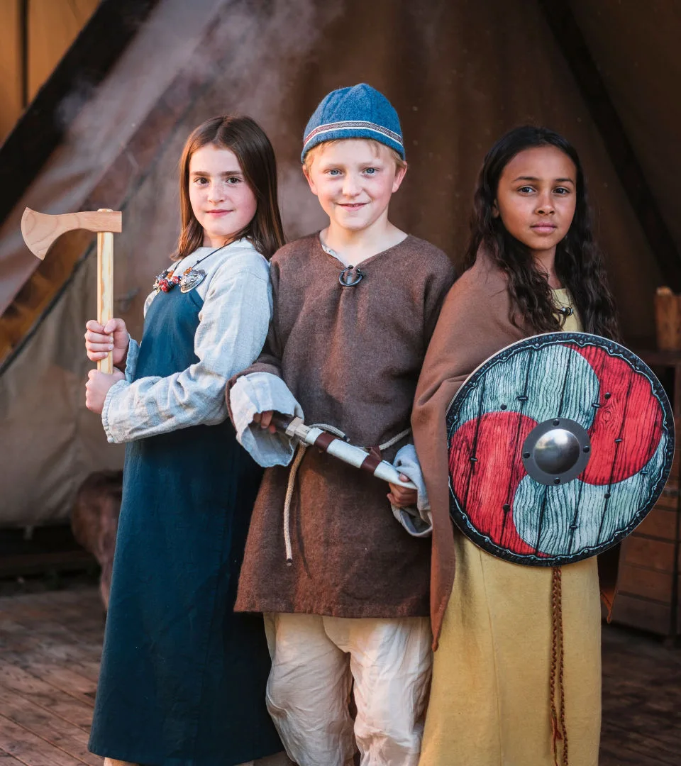 Tre barn står i vikingatida kläder.