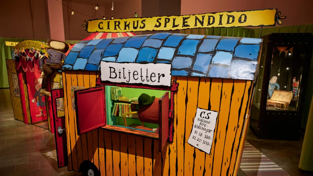 Ett gult leksakshus med blått tak och en skylt med ordet "biljetter" på.