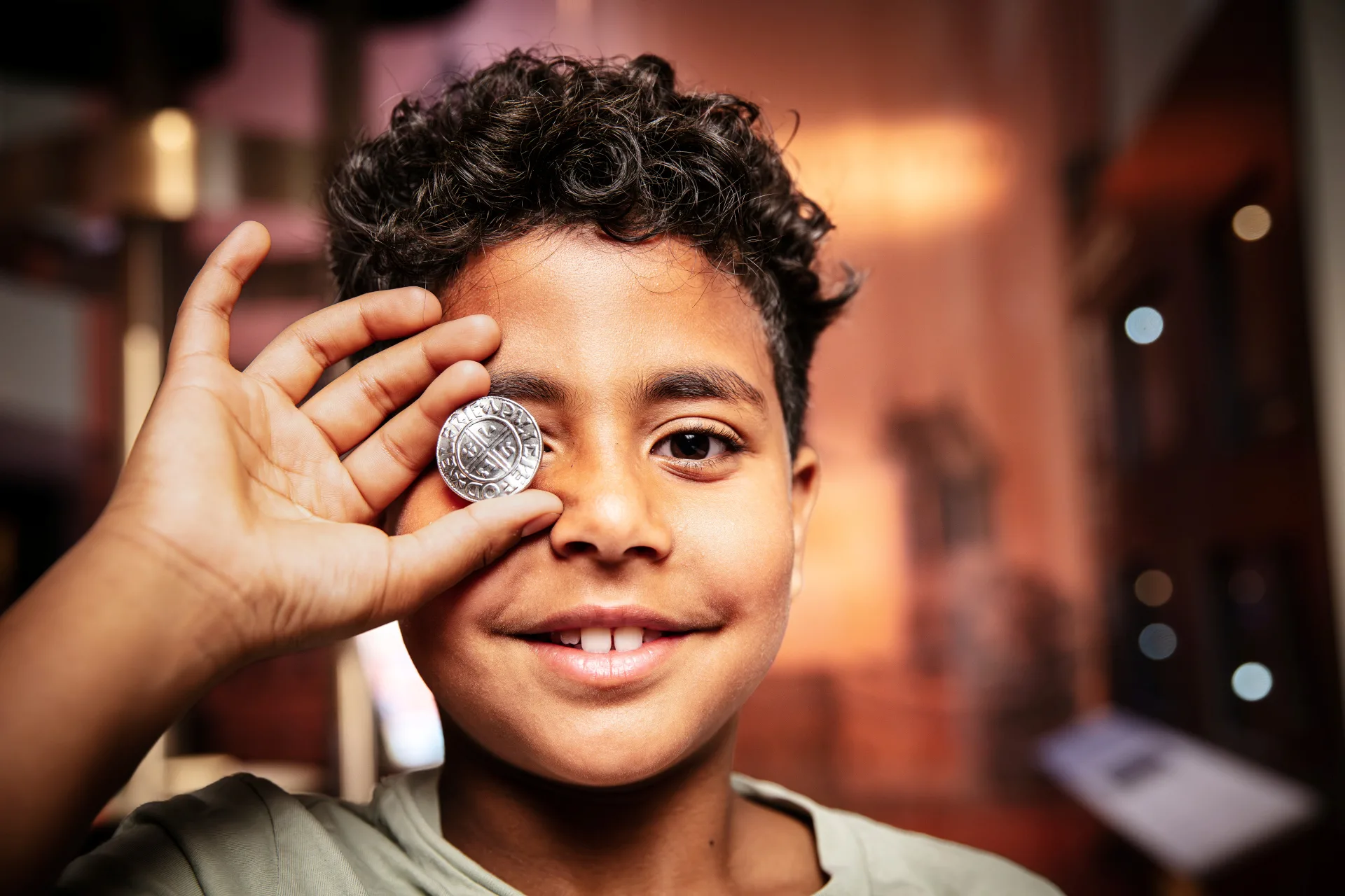 child holds a coin in front of eye